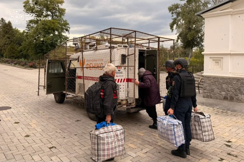 Рятувальники допомагають літнім людям сісти з речами в евакомобіль