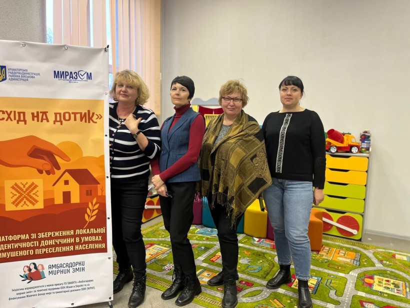 Група жінок стоїть біля банеру на якому написано «Схід на дотик».