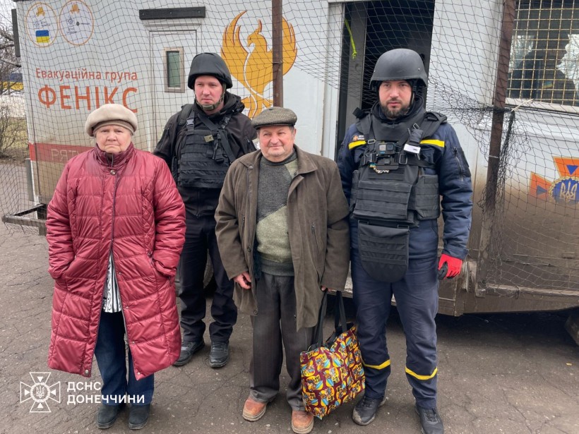 Чоловік та жінка похилого віку разом з рятувалньиками групи "Фенікс" біля евакуаційного автомобіля