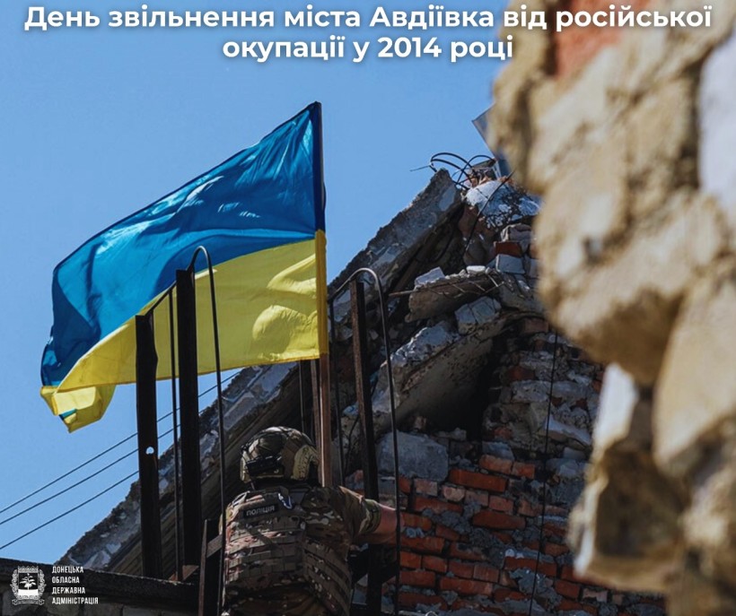 Солдат у камуфляжі піднімає український прапор на пошкодженій будівлі в Авдіївці, символізуючи звільнення, під чистим блакитним небом.