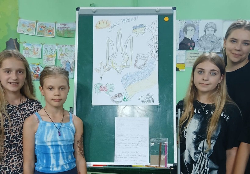 Команда дівчат презентує на дошці свою роботу, на якій зображені українські державні символи.