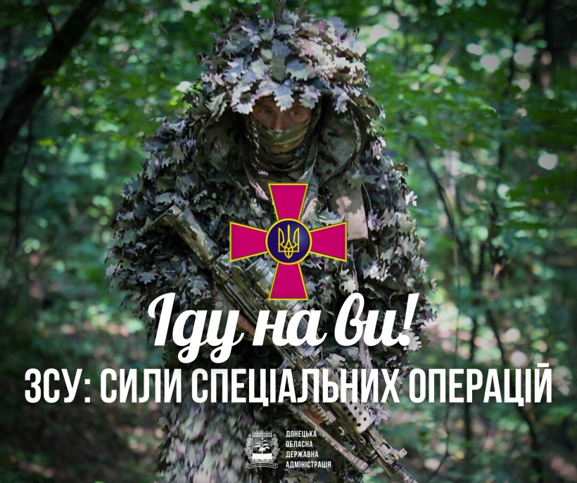 Солдат у повній камуфляжній формі стоїть у густому зеленому лісі, тримаючи гвинтівку. Українська військова емблема та напис над нею передають відчуття готовності.