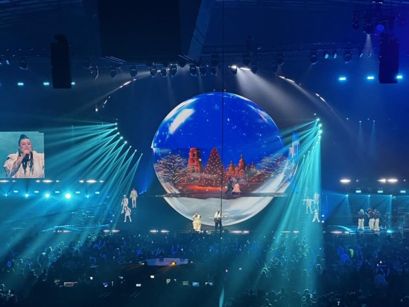 Дія на сцені концертного залу. Величезна куля, в якій відображається місто та ялинка. Співаки на сцені співають.