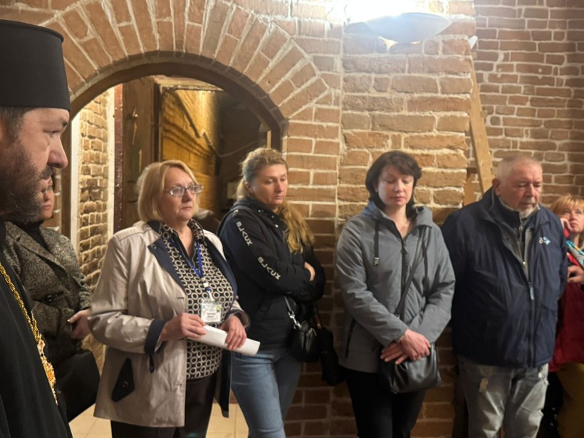 Відвідувачі та духовенство уважно слухають виступ у приміщенні з характерною цегляною кладкою стін.