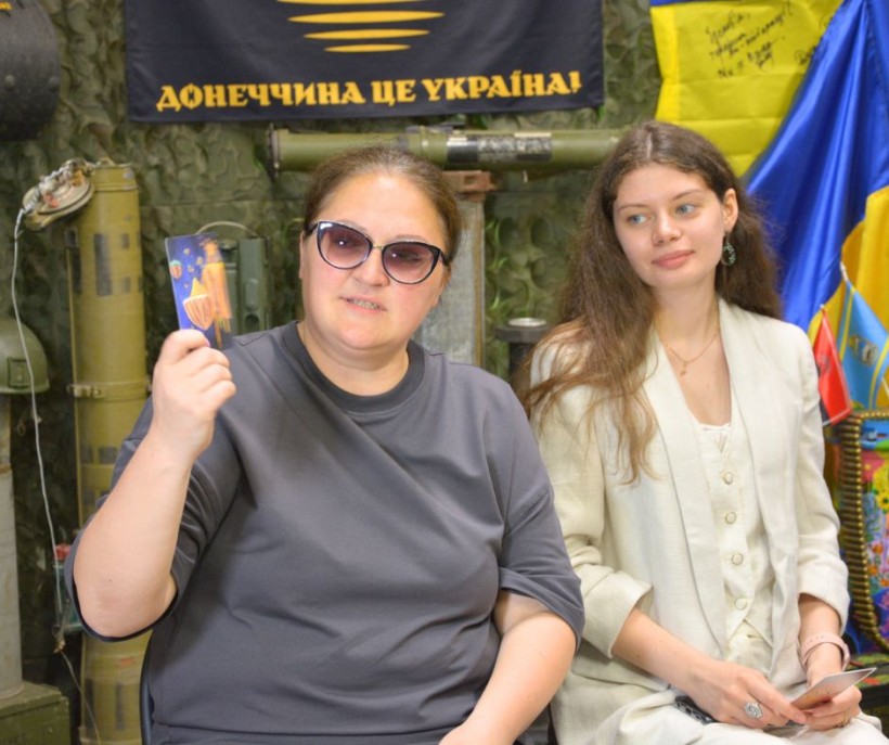 Дві учасниці зустрічі, сидять на стільцях, в руках тримають картки. Яна Штрухецька показує картку синього кольору іншим учасникам.