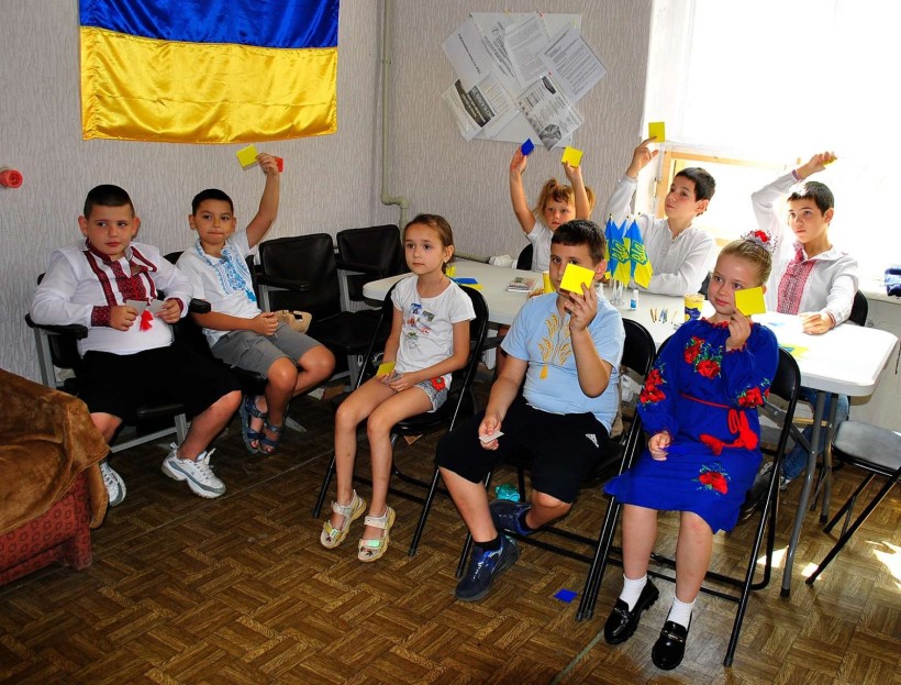 Діти беруть участь у вікторині, підіймають вгору руки з квадритиками кольорів  Державного Прапора України