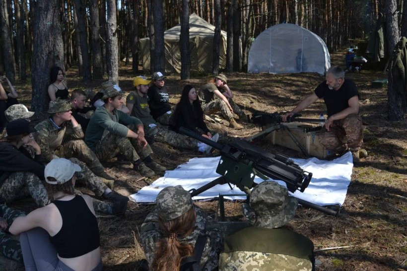 Учасники в лісі слухають інструктора під час заняття зі зброєю