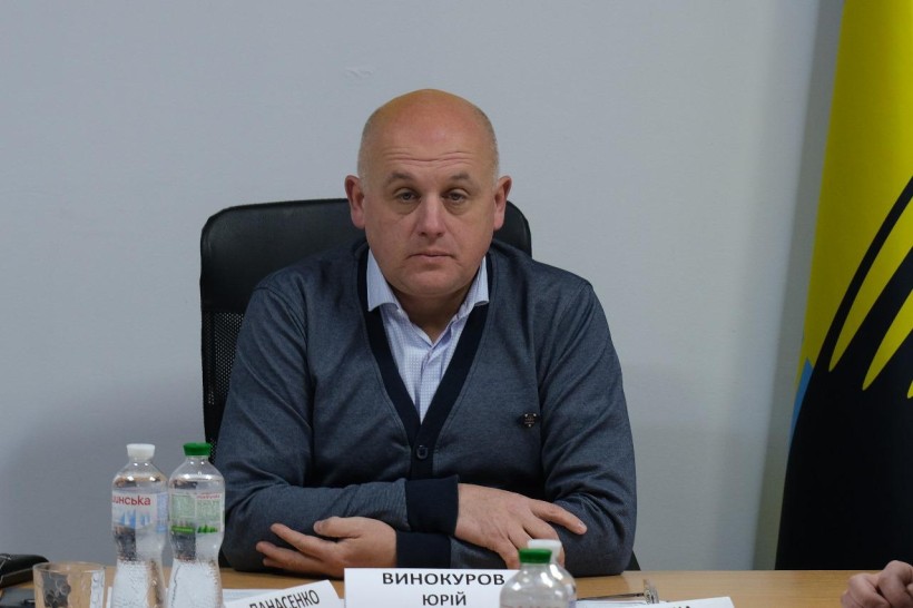 Заступник голови Донецької ОДА Юрій Винокуров, сидить за столом, поруч прапор Донеччини.