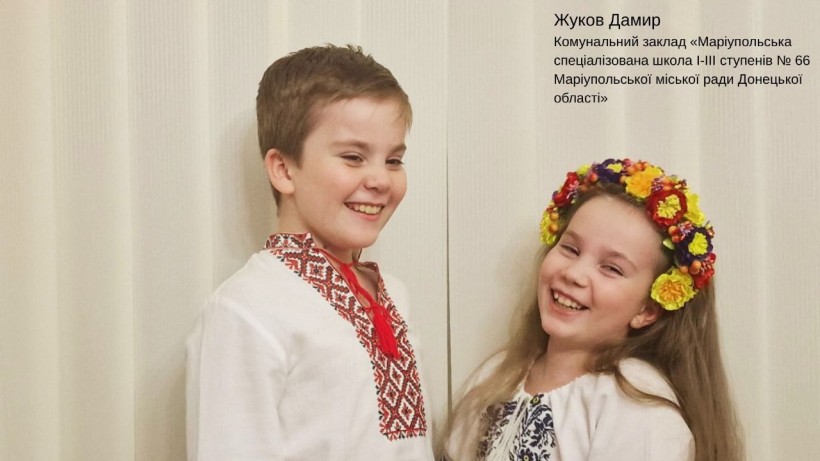 Двоє дітей, хлопчик і дівчинка, одягнені в традиційні вишиті українські сорочки та посміхаються. Дівчинка у яскравому віночку.