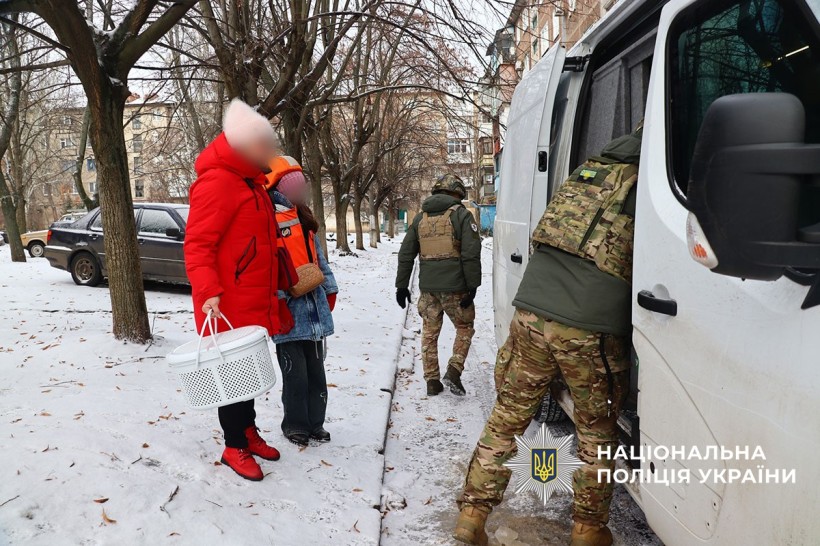 Поліцейські допомагають родині з речами. Жінка тримає кошачу переноску та дитину за руку.