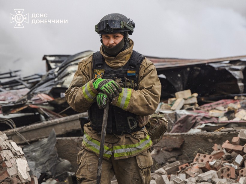 Рятувальник тримає лопату, навкруги зруйнована будівля.