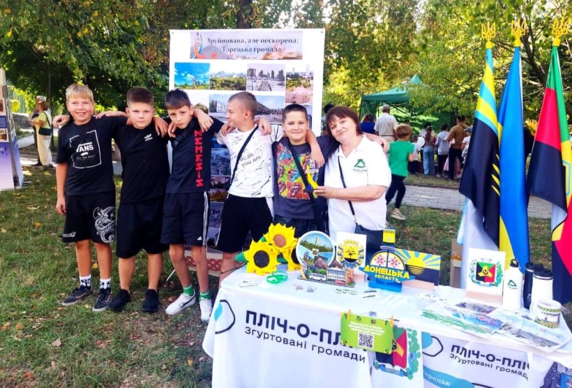 Спільне фото дітей на фоні стенда з фотографіями Торецької громади. На столі сувенірна продукція.
