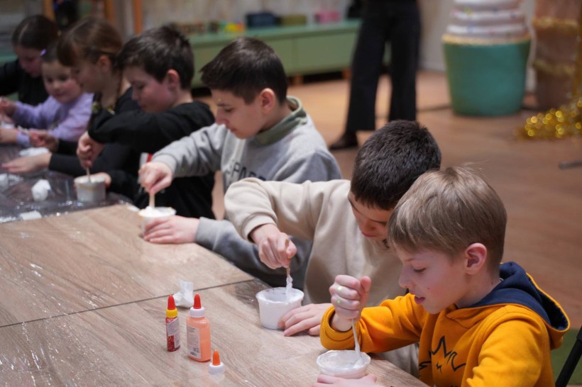 Діти зосереджено перемішують білу суміш (слайми або фарбу) у пластикових стаканчиках.