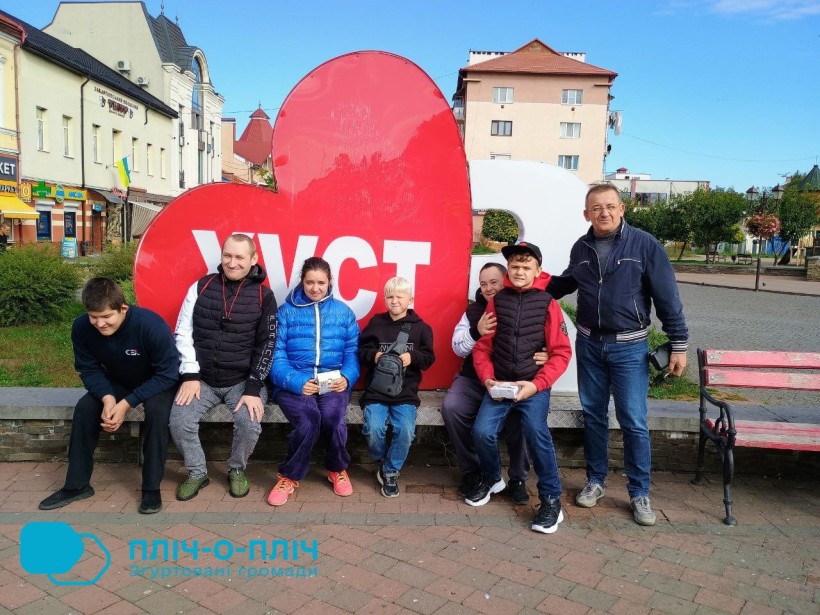 Спільне фото. Діти та дорослі біля надпису "Я люблю Хуст". Велике червоне серце на задньому плані.
