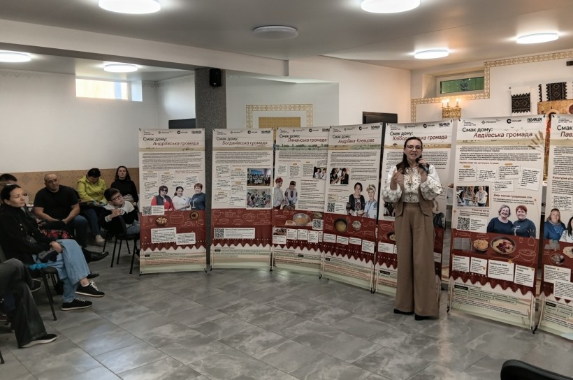 Представниця центру культури у вишиванці виступає з мікрофоном біля стенда «Смак дому: Авдіївська громада».