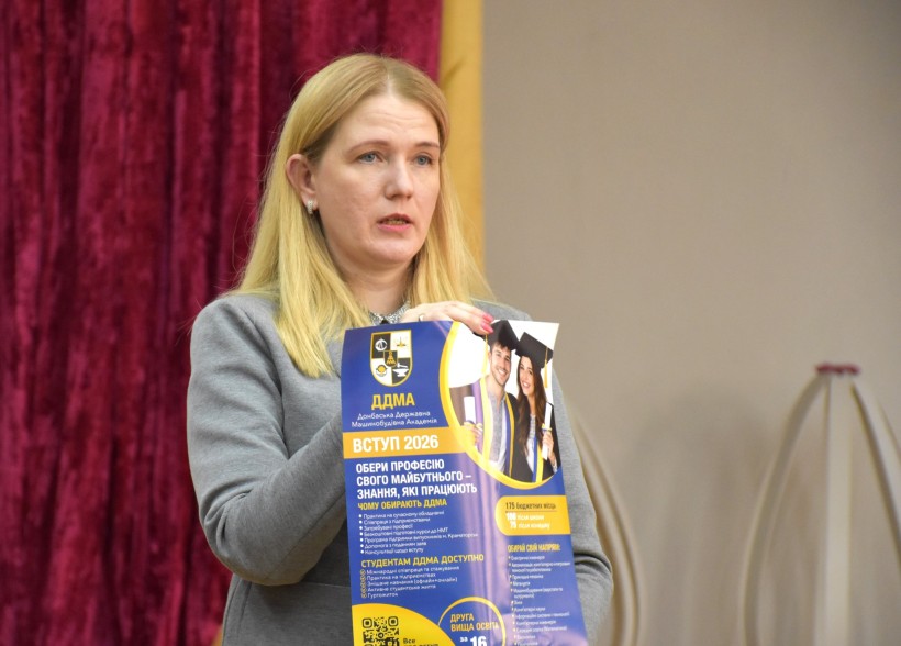 Презентація можливостей Донбаської державної машинобудівної академії та закладів професійно-технічної освіти Донеччини. Учасниця зустрічі стоїть на сцені та тримає буклет у руках.
