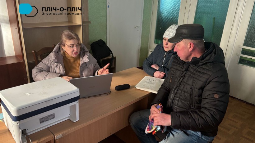 Фахівець структурного підрозділу сидить за ноутбуком, поруч мешканці громади.