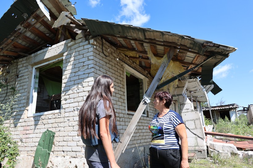 Журналіст спілкується з господинею пошкодженого будинку. На задньому плані будинок без даху та вікон.