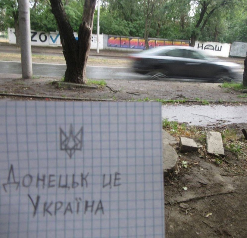 Записка сфотографована на фоні вулиці окупованого міста, на якій написано що, "Донецьк - це Україна", зверху намальований тризуб