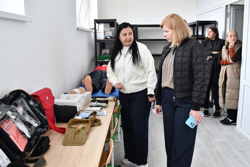 Начальник Мангушської селищної військової адміністрації Наталія Воробйова роздивляється вироби у школі мистецтв, поруч жінка щось розповідає.
