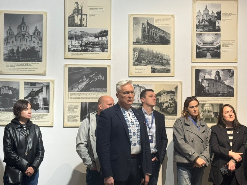 Відвідувачі виставки слухають виступи на тлі стіни з архівними чорно-білими фотографіями