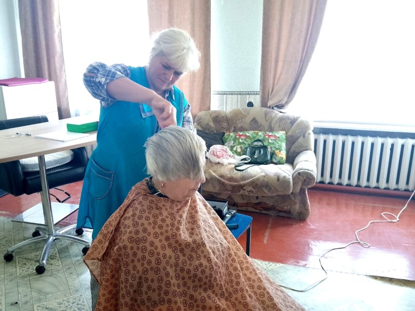 «День краси» для переселенців у селі Карабчиїв Житомирської області.
Жінка сидить з нахиленою головую, поруч перукар, яка підстригає.