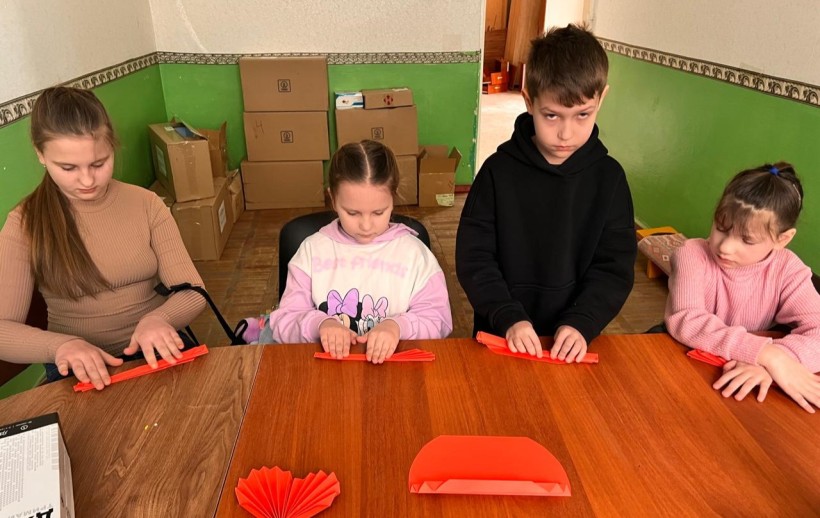 Діти Лиманщини стоять біля столу та роблять серця з червоного папіру.