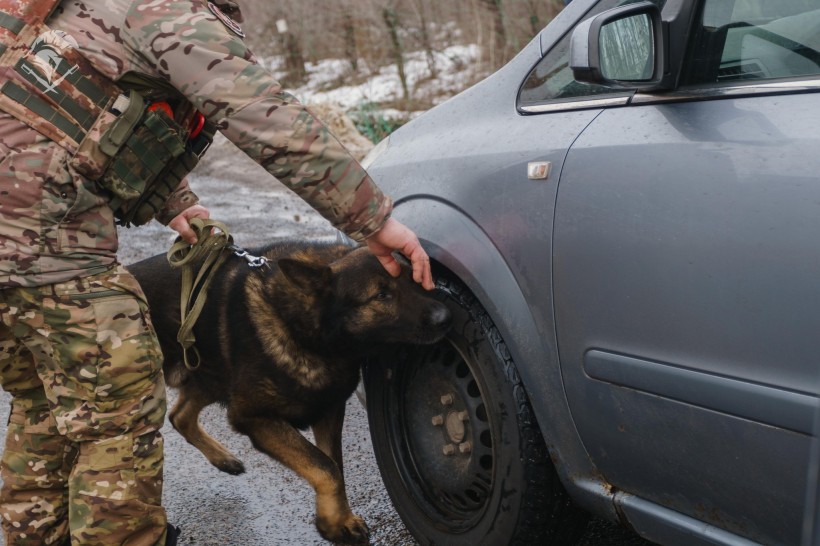 Арчі уважно оглядає переднє колесо автомобіля, поруч військовий.