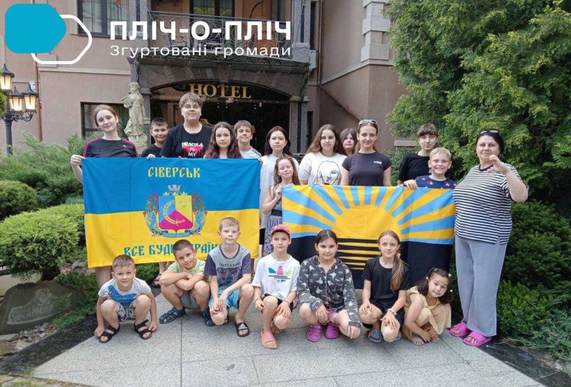 Спільне фото дітей з Сіверської громади біля входу у готель з прапорами Донеччини та Сіверська.