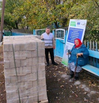 Волонтер допомагає доставити жінці палету твердопаливних брикетів