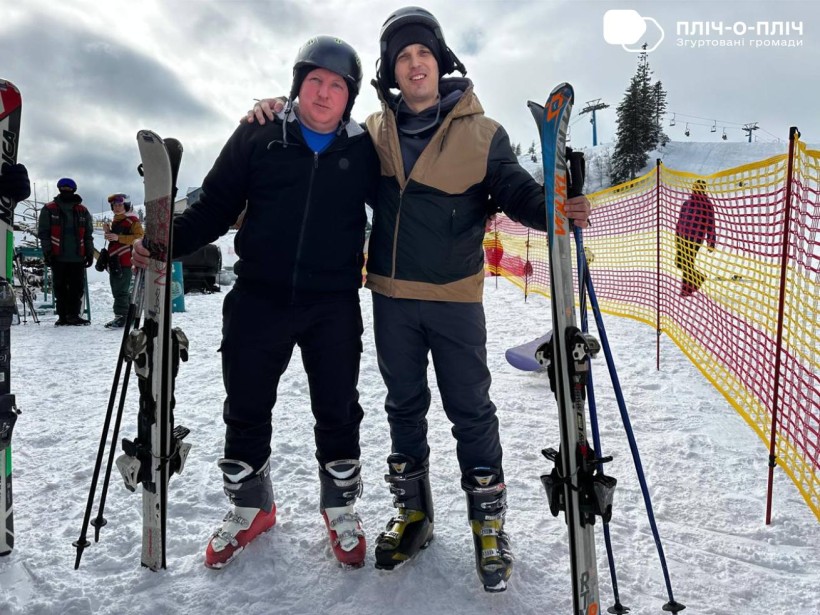 Чоловіки стоять з горнолижним приладдям. Позаду гори