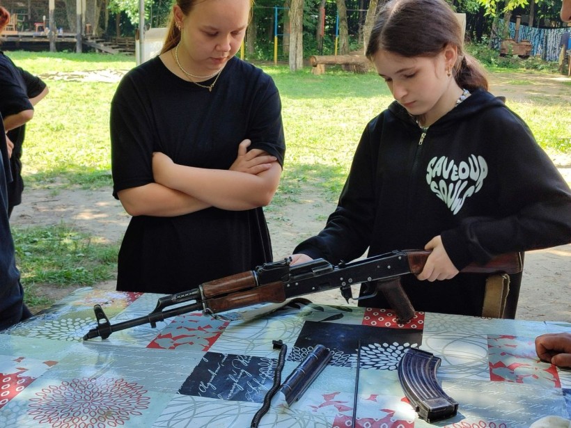 молодь табору тренується у володінні стрілецькою зброєю під наглядом наставника, відпрацьовуючи навички безпеки та поводження з автоматом.