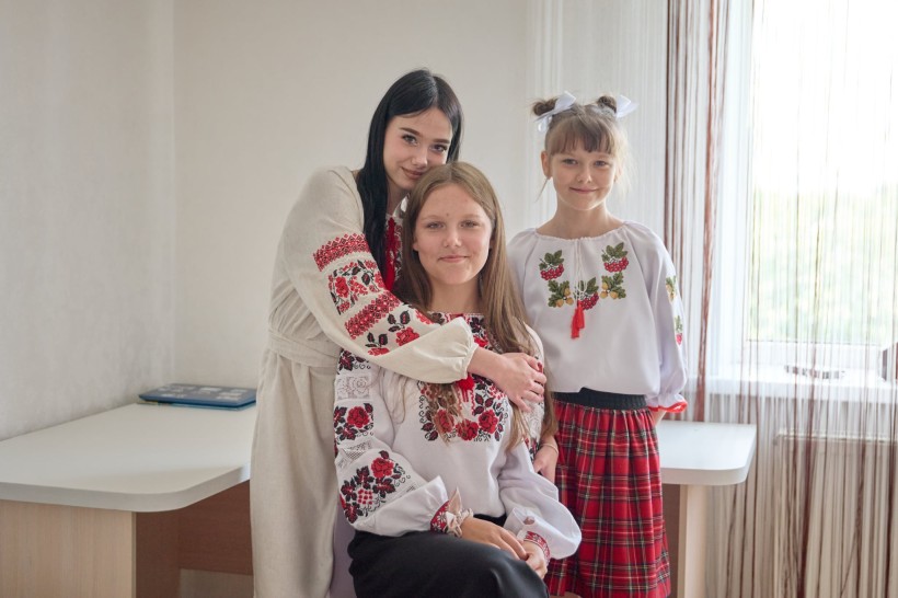 Троє дівчат у вишиванках у новій кімнаті. Одна з дівчаток обіймає іншу.