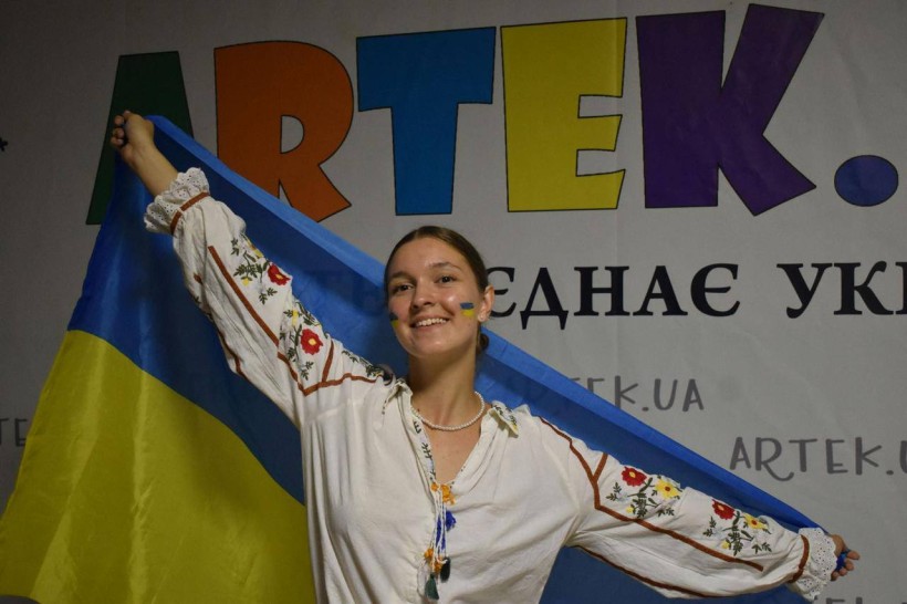 Дівчина, яка відпочиває в таборі "Артек" тримає на плечах державний прапор.