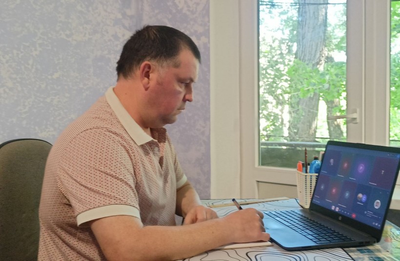Представник військової адміністрації сидить за столом та слухає доповідача на семінарі