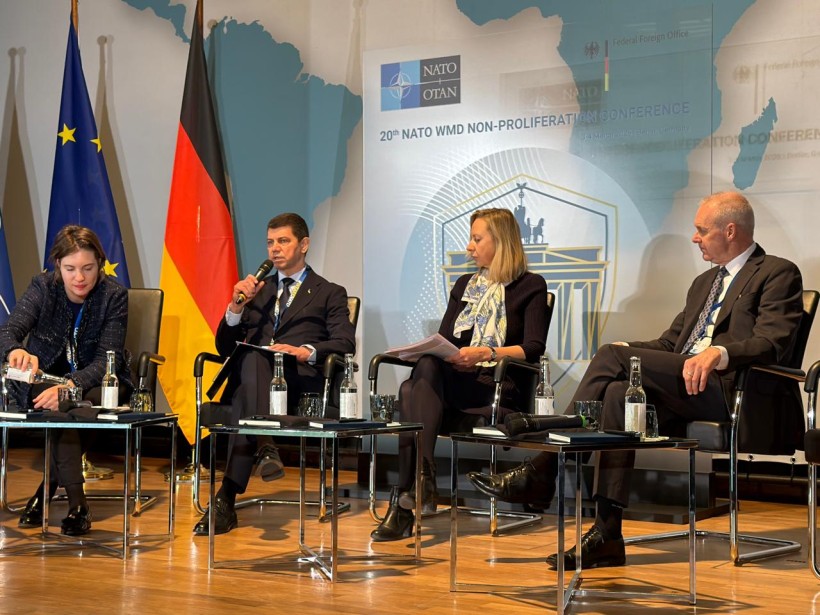 Чотири учасники 20-ї конференції НАТО з нерозповсюдження ЗМЗ сидять на сцені під час панельної дискусії в Берліні на фоні прапорів ЄС та Німеччини.