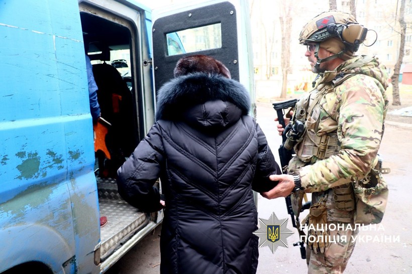 Жінка поруч з поліцейським, який допомагає їй сісти в автомобіль для евакуації