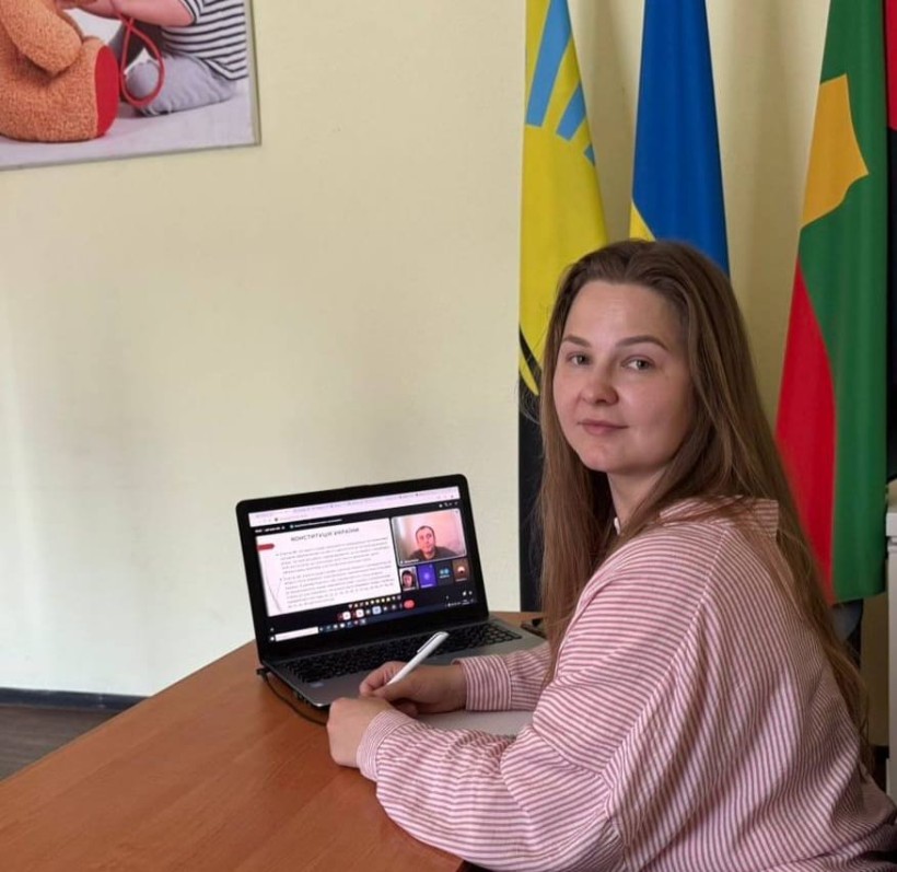 Представник військової адміністрації сидить за столом та слухає доповідача на семінарі