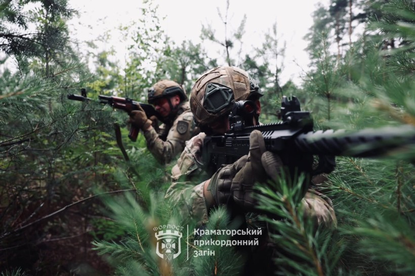 Солдати в камуфляжі та шоломах обережно пробираються густим лісом, націлюючи гвинтівки, випромінюючи напругу та зосередженість. Їх оточують соснові гілки.
