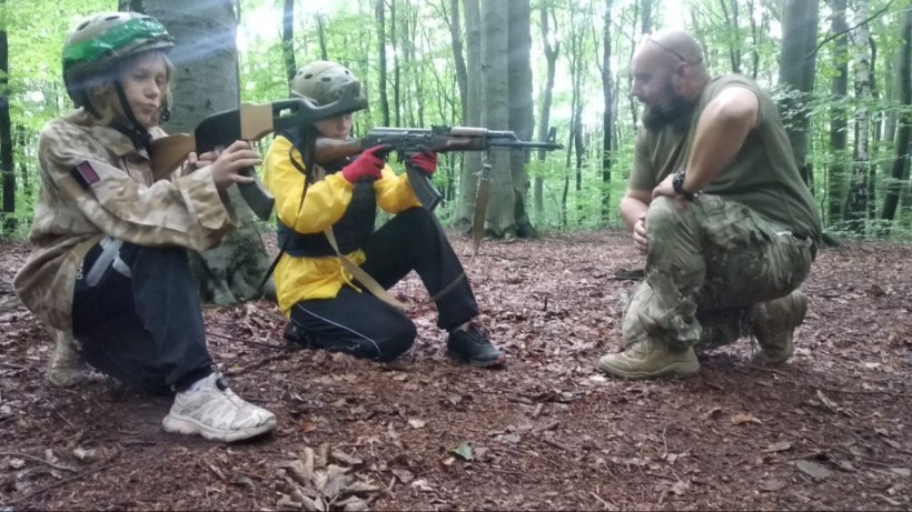 інструктор проводить заняття зі стрільби для учасників табору, навчаючи правильному положенню тіла та техніці прицілювання.