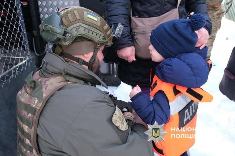Поліцейський підрозділу «Білий янгол», допомогає дитині одягнути захисний жилет для евакуації.