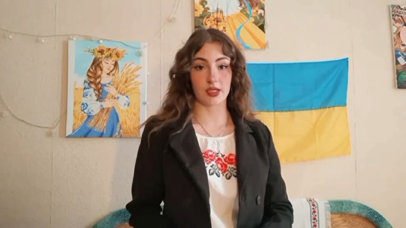 Учасниця конкурсу "Світ українською" у вишиванці на фоні картин і прапора України декламує вірш
