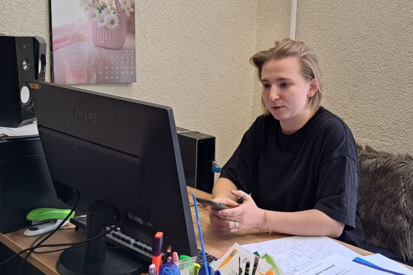 Дівчина у чорній футболці сидить за робочим столом перед монітором