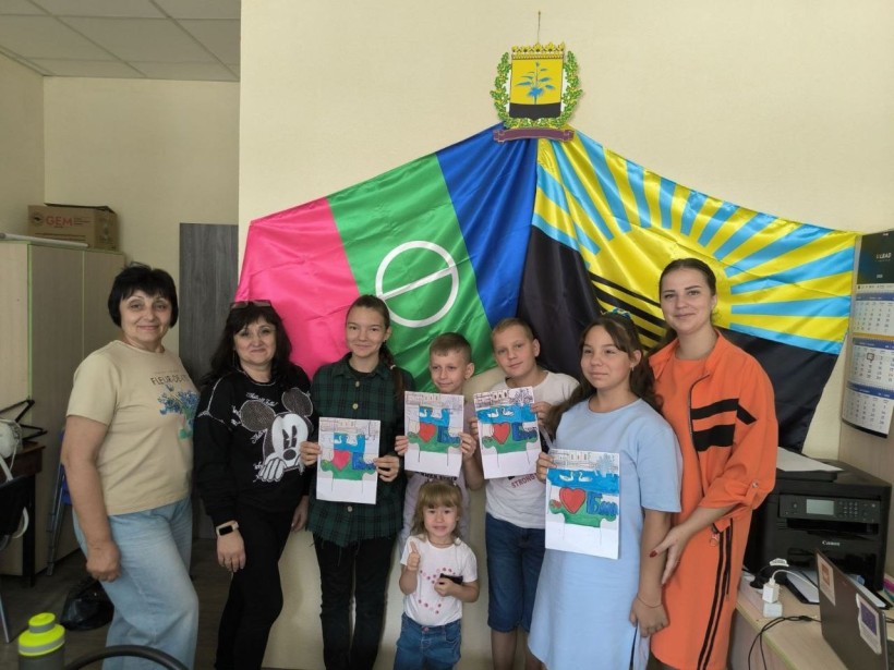 Група дітей та педагогів позує з готовими малюнками, на стіні прапори громади та області, панує відчуття гордості.