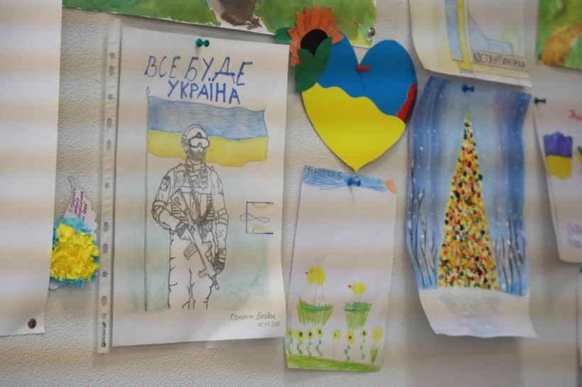 Дитячі малюнки для захисників та захисниць. Жовто- блакитне серце, захисник, позаду якого прапор України.