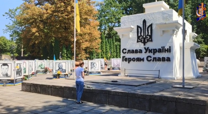 Учасниця акції стоїть біля меморіалу загиблим воїнам, де розміщено багато фотографій