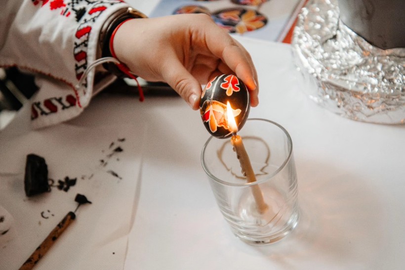 Розписана писанка, яку тримають біля свічки.