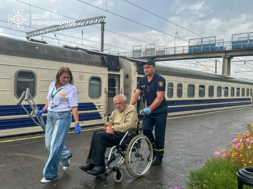 Евакуаційний потяг привіз на Рівненщину людей. Чоловіка на кріслі колісному на вокзалі везуть рятувальник ДСНС та представниця благодійної організації