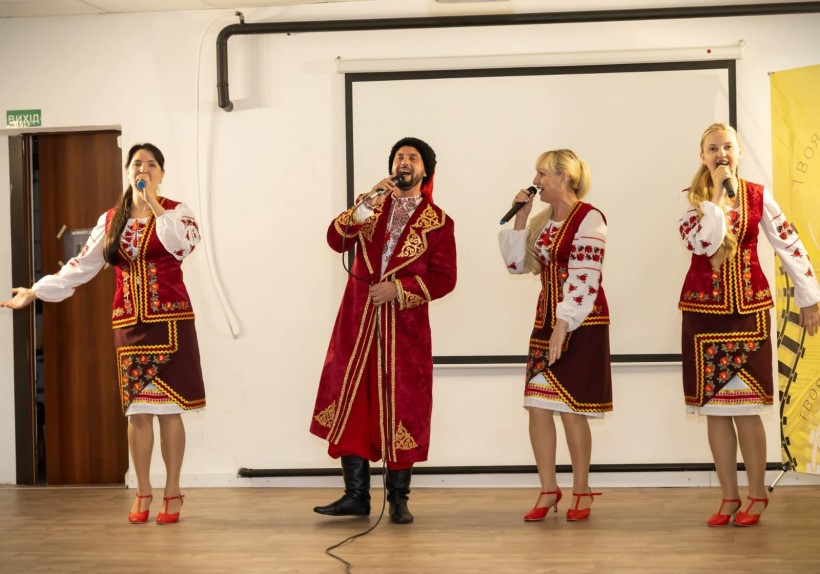 Дівчата у національному вбранні та хлопець у козацькому костюмі співають на сцені.