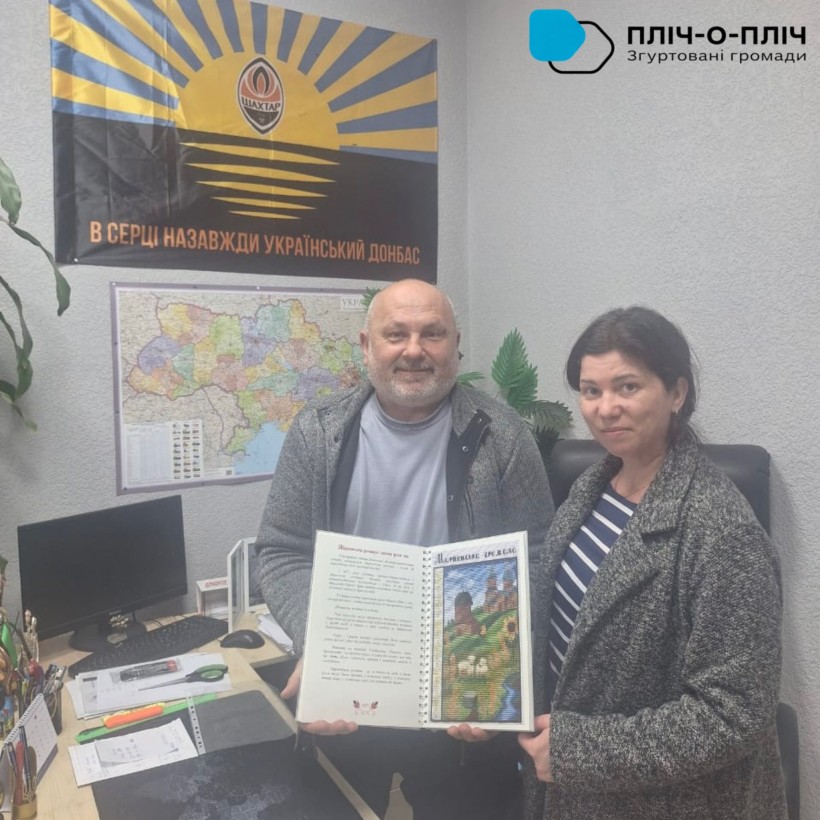 Заступник начальника Мирненської селищної військової адміністрації Василина Ніколаєва  передає книгу "Донеччина вишивана" голові Великолучківської громади